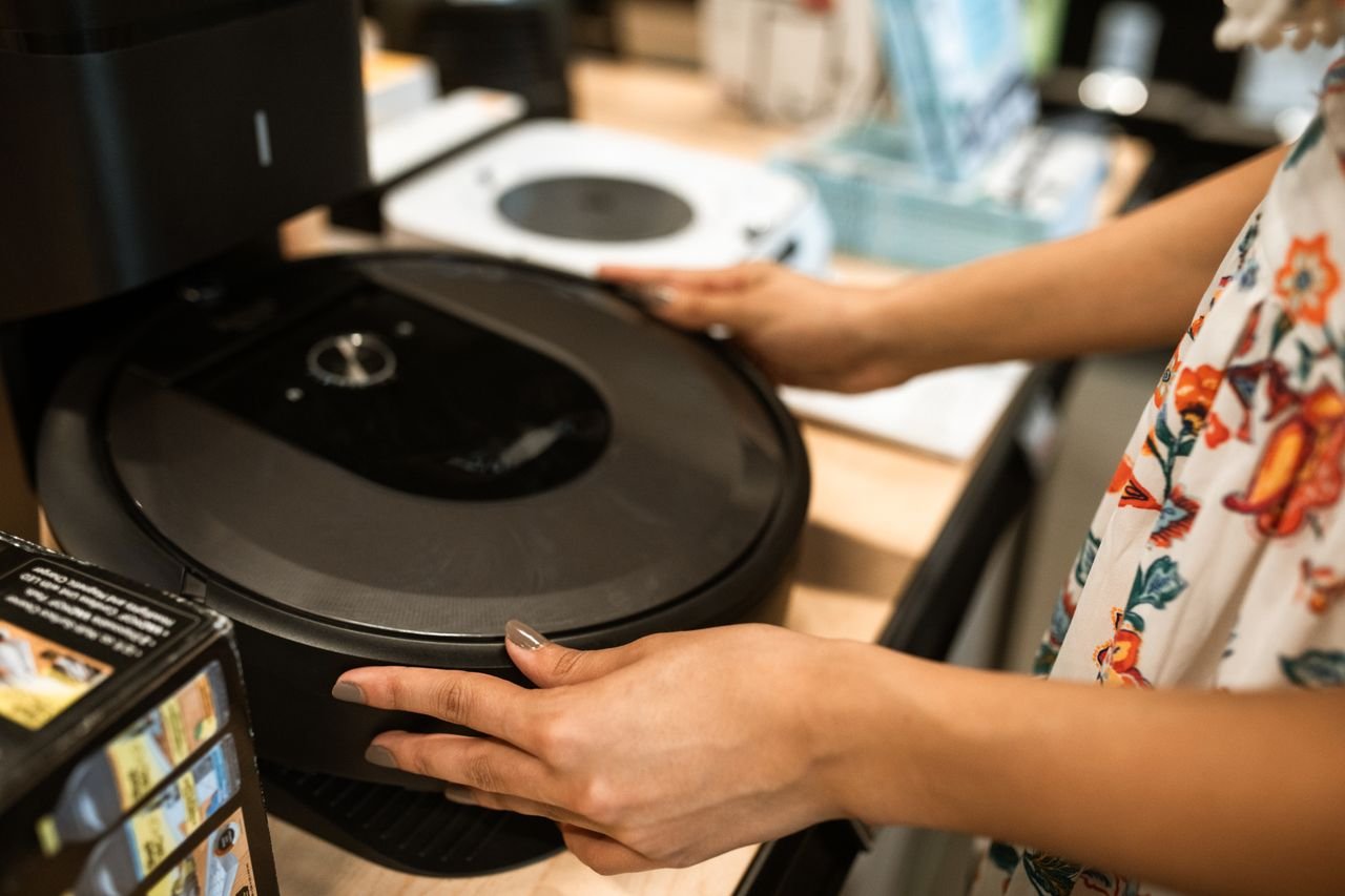 Services A customer examines a sleek robotic vacuum cleaner in a modern store.