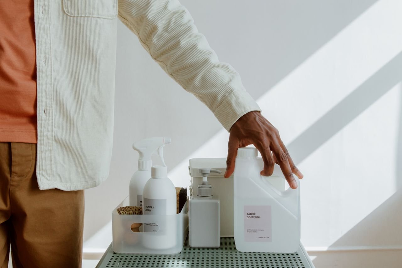 Mastering the First Impression: Your intriguing post title goes here Close-up of a man holding fabric softener surrounded by cleaning products in a minimalist setting.